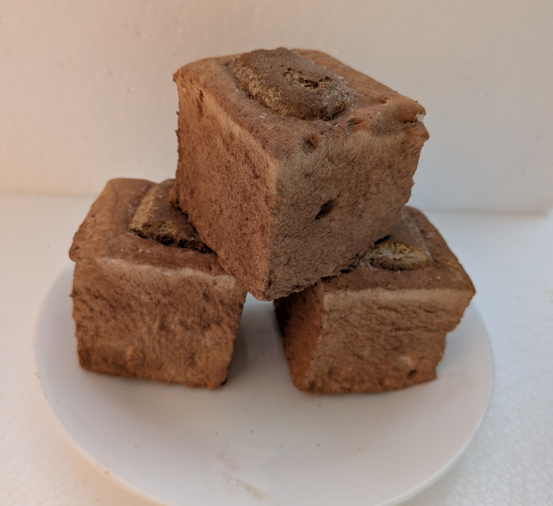 Three square pieces of Tiramisu Gourmet Marshmallowsstacked on a white plate with a white background