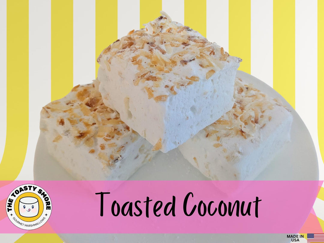 Handcrafted toasted coconut marshmallows made with beef gelatin, organic marshmallow root, and no corn syrup, displayed against a vibrant yellow and white striped background. Each marshmallow measures approximately 2" x 2" x 1.5", showcasing a soft, fluffy texture with golden coconut flakes. The Toasty S’more logo and a “Made in USA” flag highlight artisanal quality and American craftsmanship.