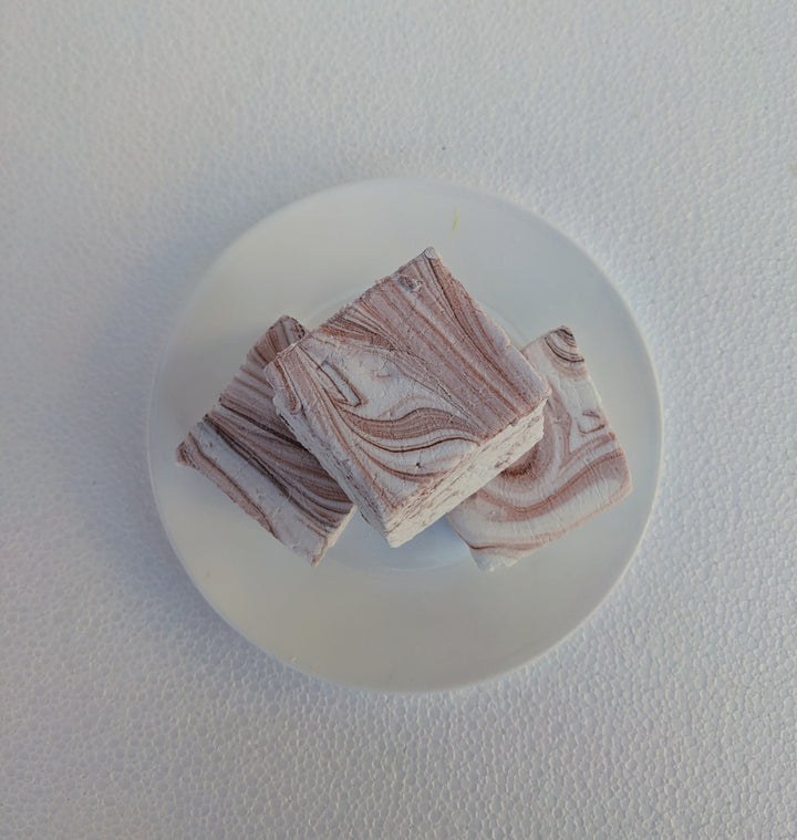 A top-down view of coffee-flavored gourmet marshmallows, handcrafted and made in the USA by The Toasty Smore, arranged on a white plate. Each marshmallow is white with rich brown swirls, creating a marbled effect that highlights the bold coffee infusion. The overhead perspective showcases their soft, fluffy texture and intricate swirls, emphasizing their artisanal quality. Perfect for coffee lovers, these best gourmet marshmallows offer a delicious balance of sweetness and deep coffee flavor, ideal for pair