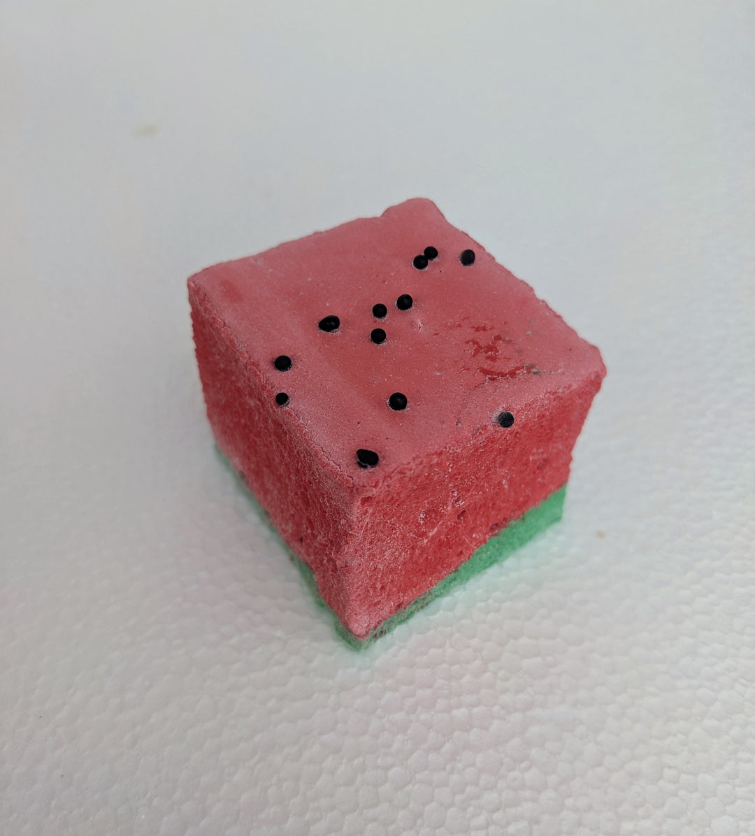 A close-up view of a single watermelon-inspired gourmet marshmallow, handcrafted and made in the USA by The Toasty Smore. The marshmallow features a green base and a red top, designed to resemble a juicy watermelon slice. Tiny black sprinkles are scattered across the red layer, mimicking watermelon seeds. The soft, fluffy texture and vibrant colors make it one of the best fruity marshmallows, perfect for a fun and delicious treat.