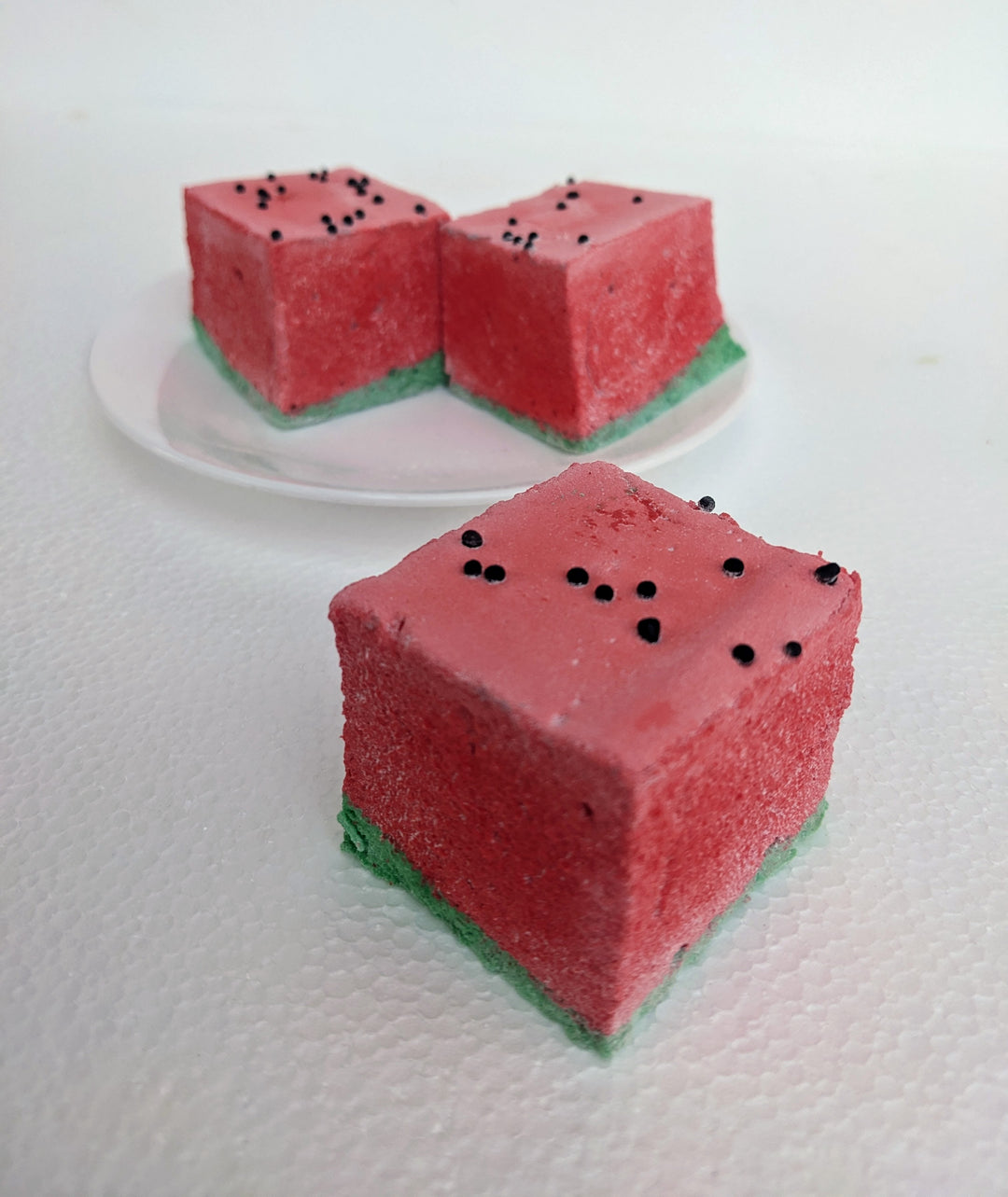 A close-up view of three watermelon-inspired gourmet marshmallows, handcrafted and