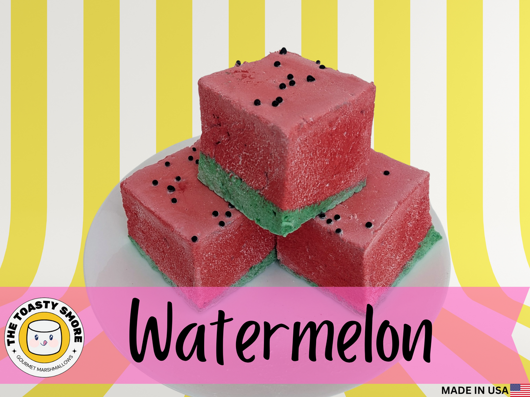 three watermelon-themed gourmet marshmallows arranged on a white plate. Each marshmallow has a green bottom layer and a red top layer, mimicking the look of a fresh watermelon slice. Tiny black sprinkles are scattered across the red portion, resembling watermelon seeds. The soft, fluffy texture and vibrant colors create a playful, summery aesthetic, highlighting their handcrafted quality and delicious appeal.