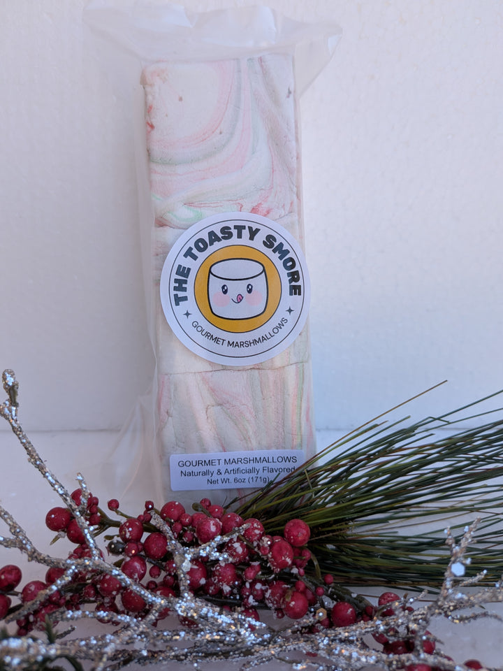 Packaged White Chocolate Peppermint Bark marshmallows by The Toasty S’more, styled with festive Christmas branches. Handcrafted, corn-syrup free, and made with beef gelatin and organic marshmallow root for a clean-label holiday indulgence.
