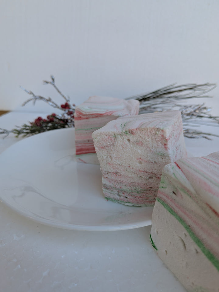 Three White Chocolate Peppermint Bark marshmallows by The Toasty S’more arranged in a line, styled with festive Christmas branches on a clean white background. Handcrafted with beef gelatin and organic marshmallow root for a corn-syrup free, clean-label holiday treat.