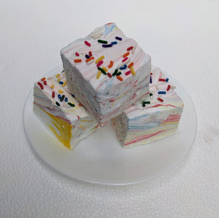 Three vibrant Tutti Frutti gourmet marshmallows with colorful swirls of fruity flavors, each topped with Rainbow sprinkles. Set against a clean white background, the marshmallows' soft, pillowy texture contrasts with the candy-coated crunch, creating a visually appealing and playful treat.