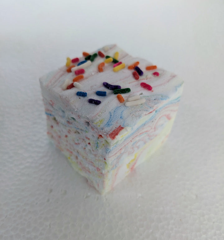 one vibrant Tutti Frutti gourmet marshmallows with colorful swirls of fruity flavors, topped with Rainbow sprinkles. Set against a clean white background, the marshmallows' soft, pillowy texture contrasts with the candy-coated crunch, creating a visually appealing and playful treat.