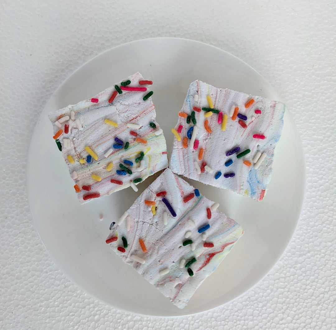 top view of Three vibrant Tutti Frutti gourmet marshmallows with colorful swirls of fruity flavors, each topped with Rainbow sprinkles. Set against a clean white background, the marshmallows' soft, pillowy texture contrasts with the candy-coated crunch, creating a visually appealing and playful treat.