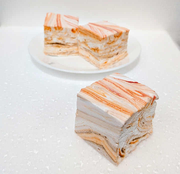 Layered pumpkin chai gourmet marshmallows with orange and white stripes on a white plate.