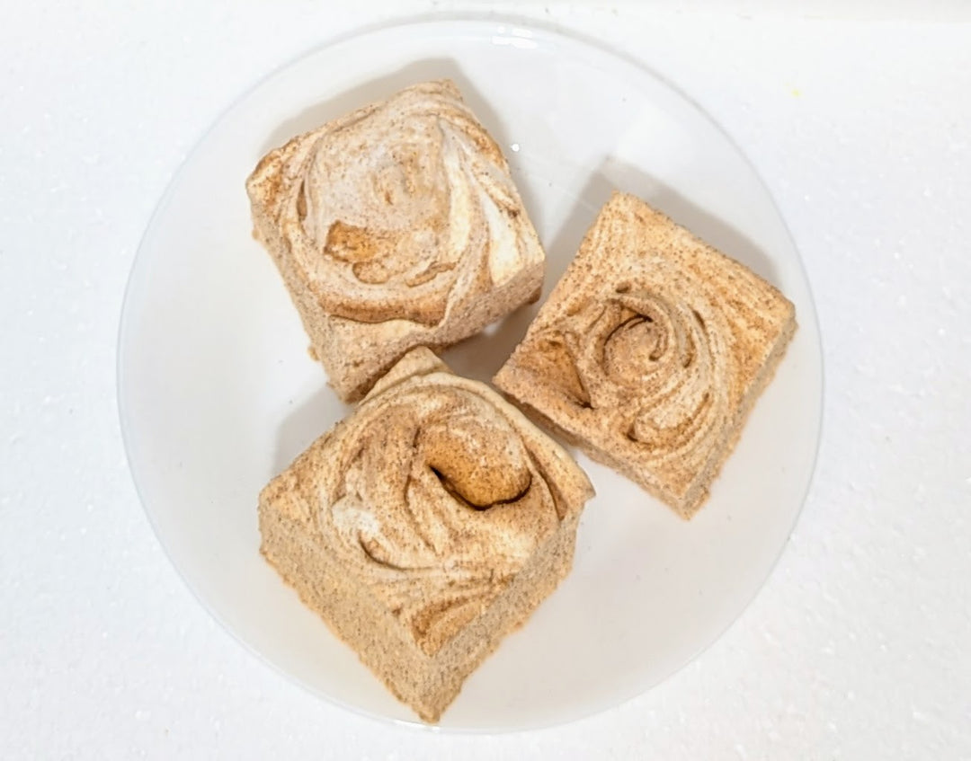 Three square pieces of cinnamon roll marshmallows with a swirl pattern on a white plate.