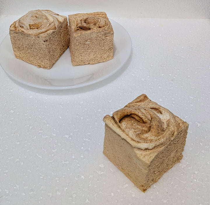 Two square pieces of gourmet marshmallows that is cinnamon roll with a swirl pattern on a white surface.