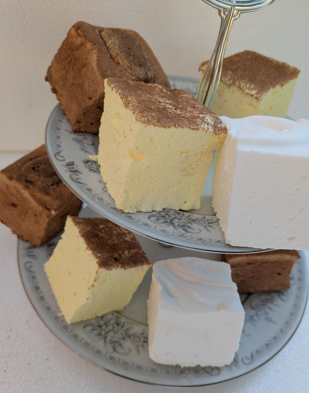 Three-tiered cake stand with slices of different types of gourmet marshmallows on a white surface.