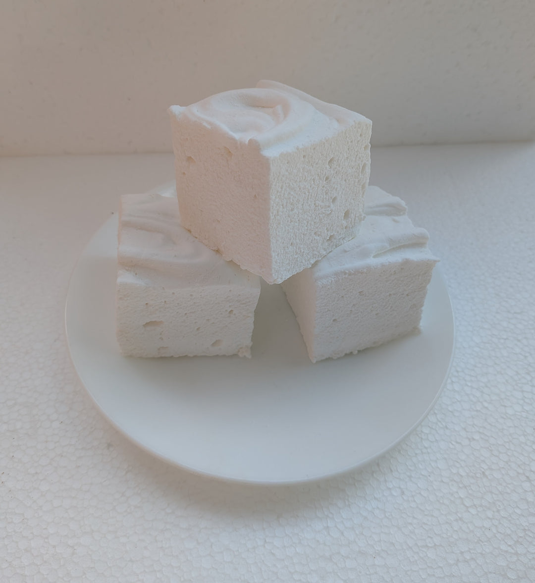 Three white marshmallows stacked on a white plate with a white background
