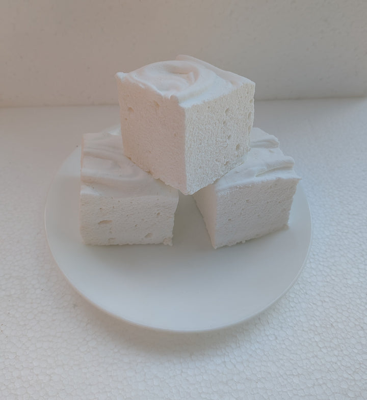 Three white marshmallows stacked on a white plate with a white background