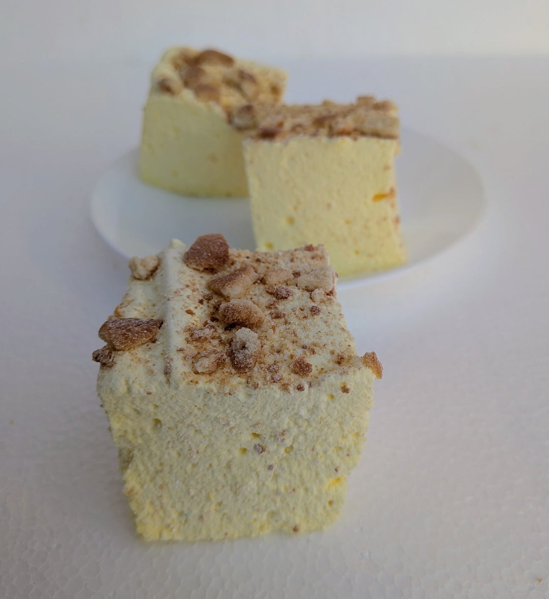 Three pieces of Banana Cream Pie gourmet marshmallows made with organic marshmallow root and premium beef gelatin, topped with a crumbly topping, on a white plate.