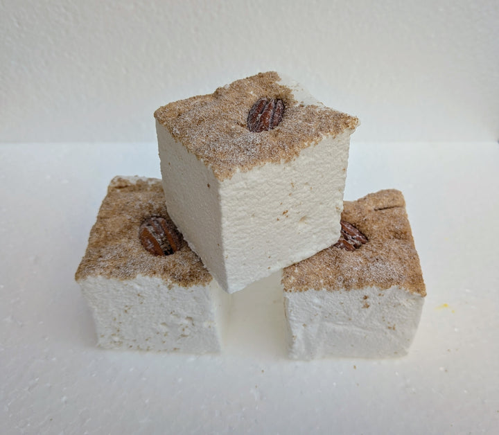 Three maple pecan pie gourmet marshmallows with cinnamon sugar and a pecan on top, stacked on a white surface.