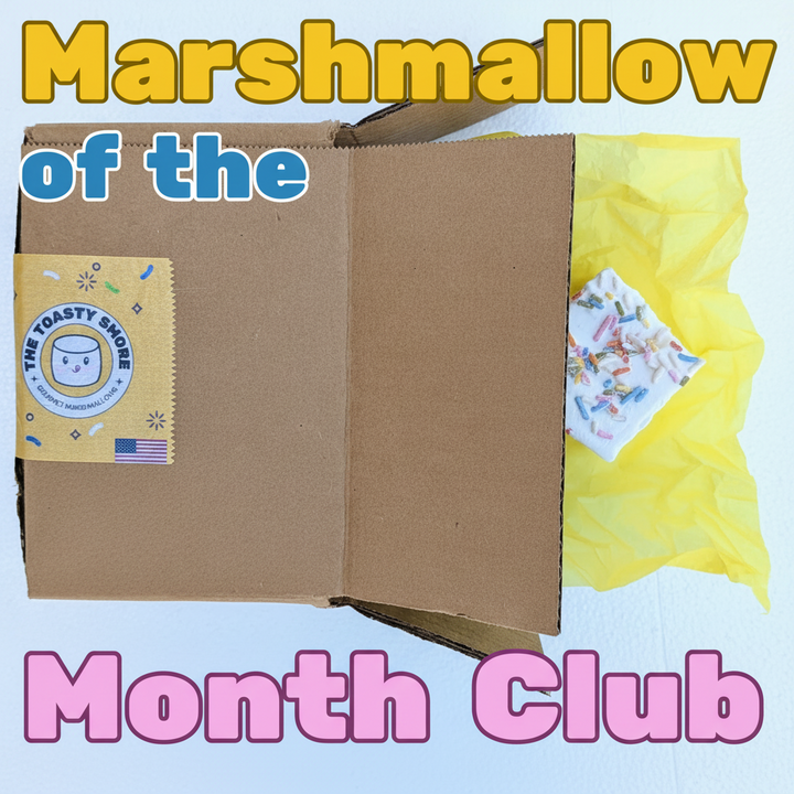 Marshmallow of the Month Club subscription box with a handmade 2‑inch gourmet marshmallow peeking out of a brown kraft box lined with yellow tissue paper, made with beef gelatin and organic marshmallow root, corn‑syrup free and small‑batch crafted by The Toasty S’more.