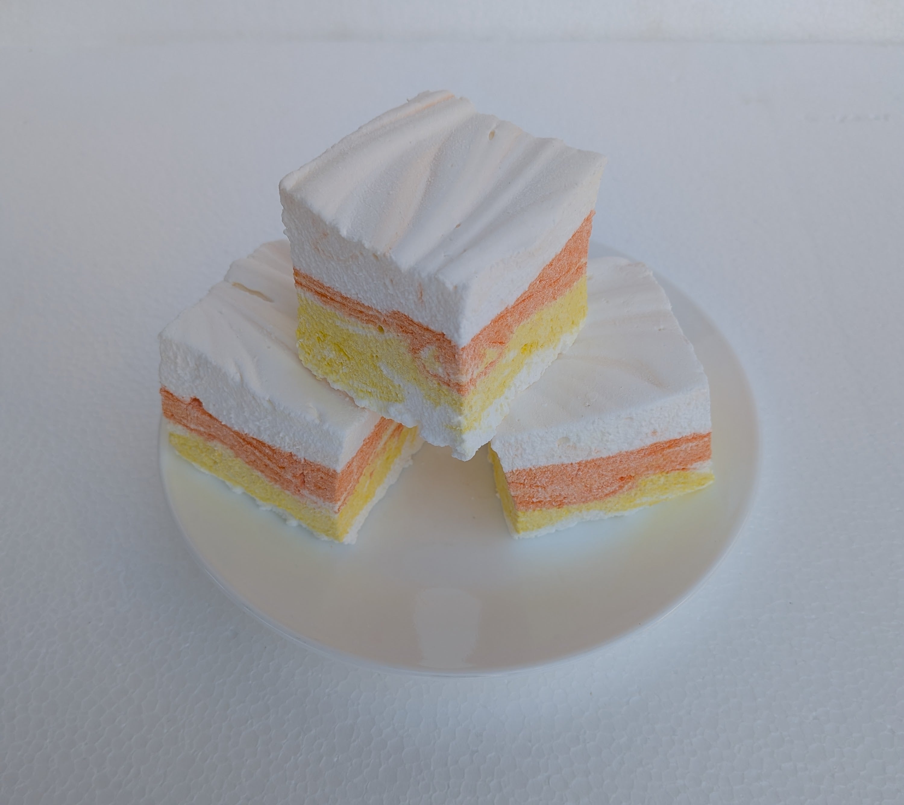 Three-layered Candy Corn gourmet marshmallows made with organic marshmallow root, arranged on a white plate against a white background