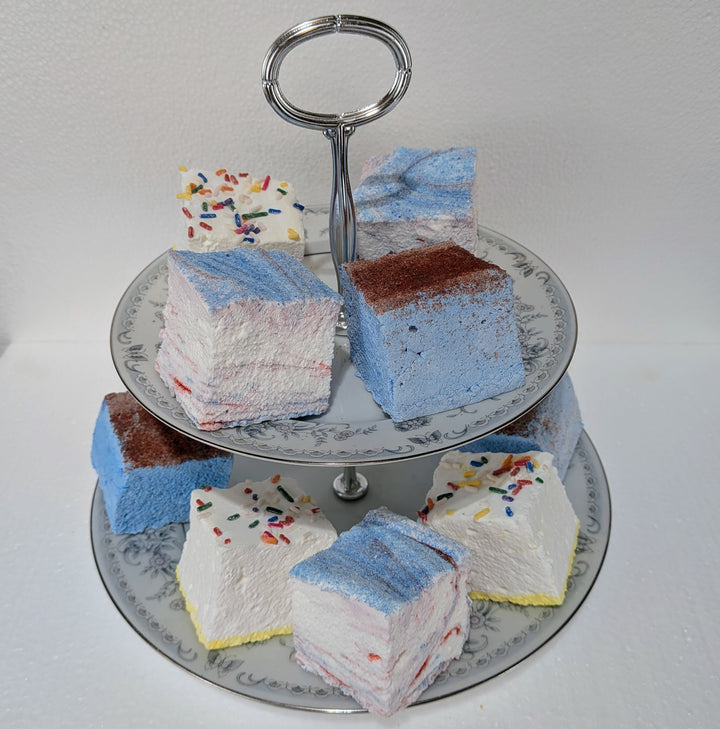 Colorful layered party favorites bundle gourmet marshmallows slices on a two-tiered stand against a plain background