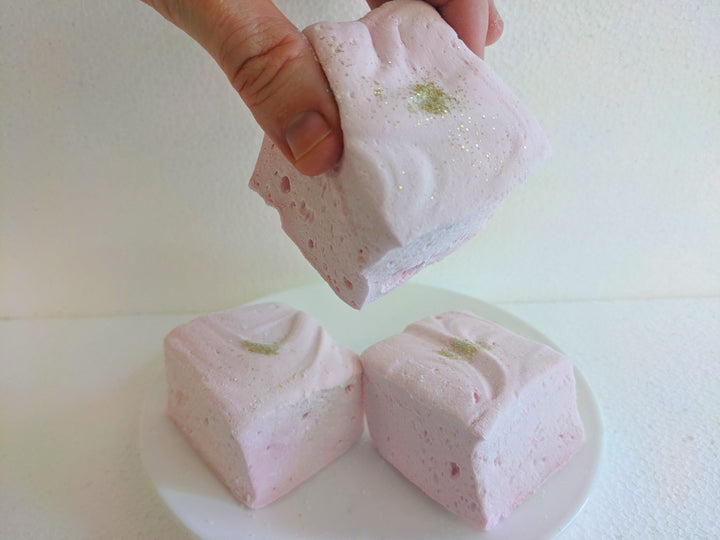 Plate of Champagne and Sugar Flavored Gourmet Marshmallows being picked up to show the large size with a white background