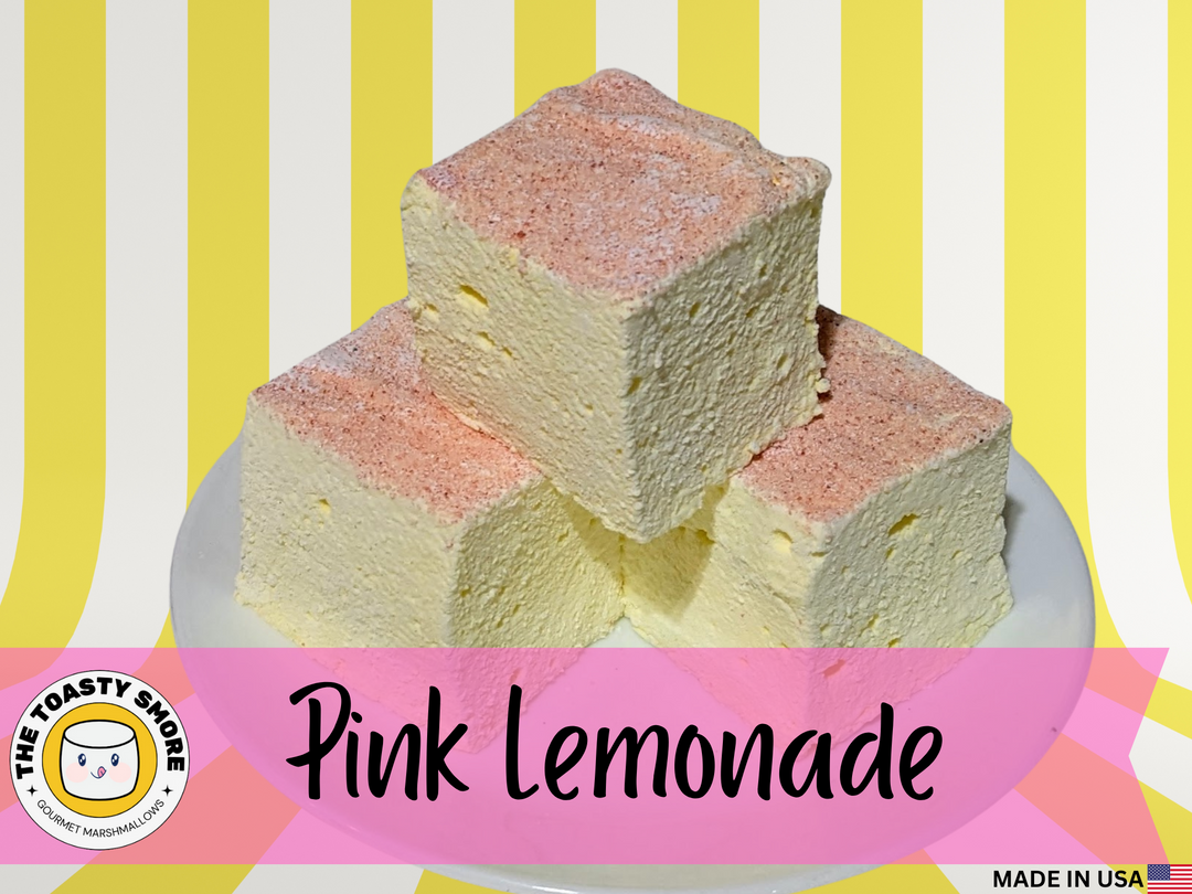 Three fluffy pink lemonade gourmet marshmallows, each a soft 2-inch cube with subtle yellow and blush pink tones, rest neatly on a white plate, creating a clean and inviting visual contrast.