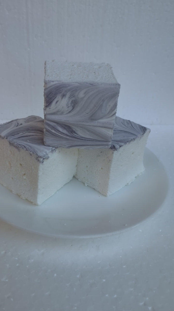 Video showing a hand placed behind a Creamy Taro marshmallow for scale, highlighting its white base and purple swirled top, made in the USA with Halal‑certified beef gelatin, organic marshmallow root, natural dyes, no corn syrup, and gluten‑free ingredients from The Toasty S’more.