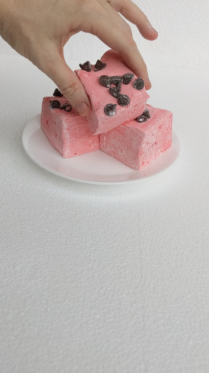 A hand picks up a Gourmet Handcrafted Wild Cherry Chip Marshmallow and squeezes it for a squish test