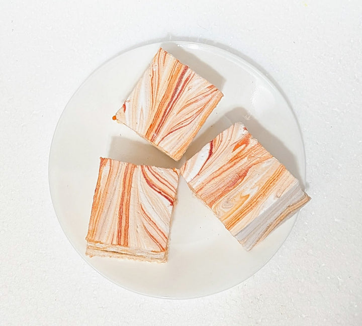 Three slices of marble-patterned pumpkin chai gourmet marshmallows on a white plate with a white background