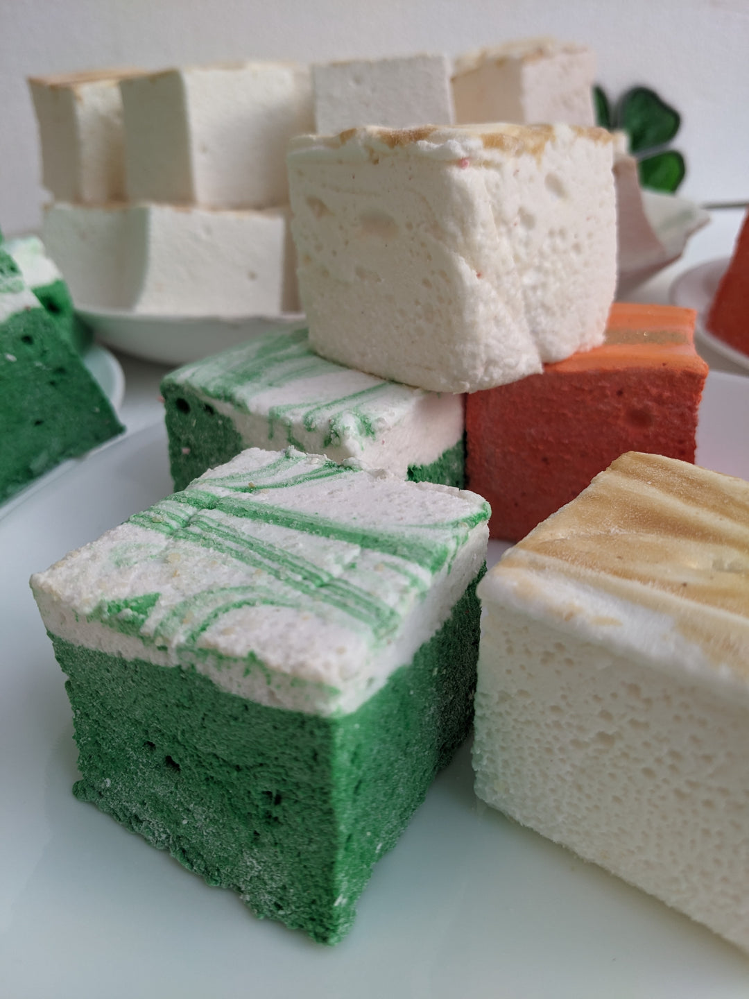 A festive plate displaying green, cream, and gold gourmet marshmallows in St. Patrick's Day flavors: Irish Cream, Green Ginger Beer, and Golden Butterscotch.