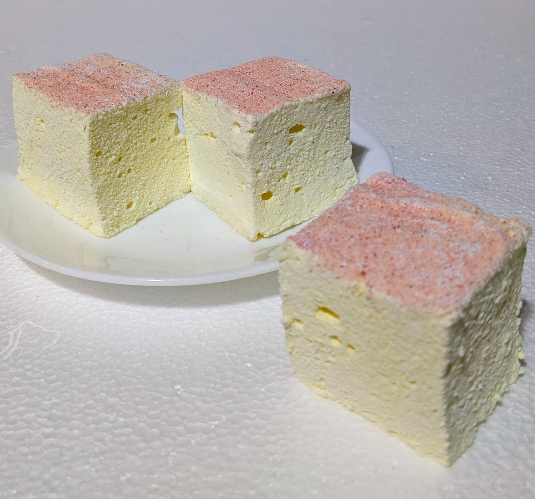Pink lemonade gourmet marshmallows—2-inch handcrafted cubes—displayed on a simple white plate, highlighting their delicate color and airy texture.