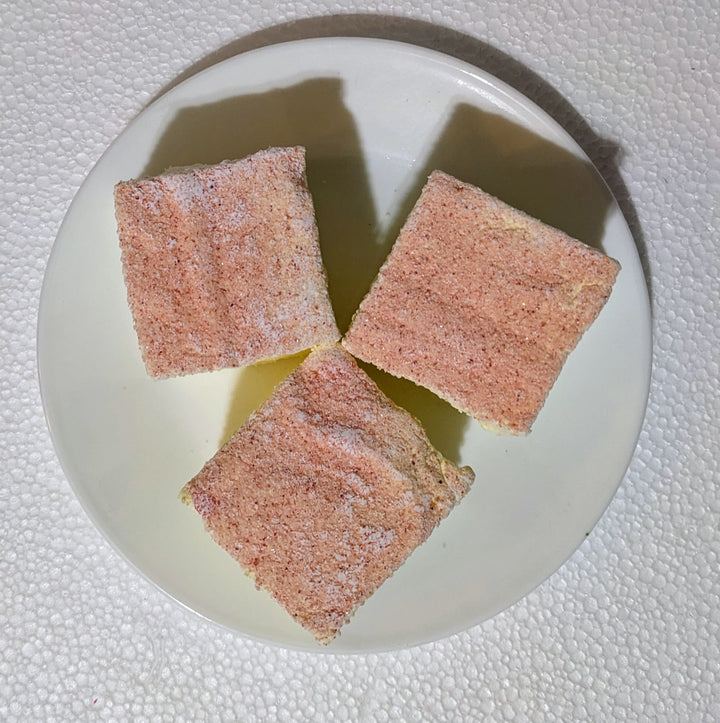 A trio of fluffy, pastel pink and yellow gourmet marshmallows sits on a white plate, capturing the soft, lemony sweetness in every airy swirl.