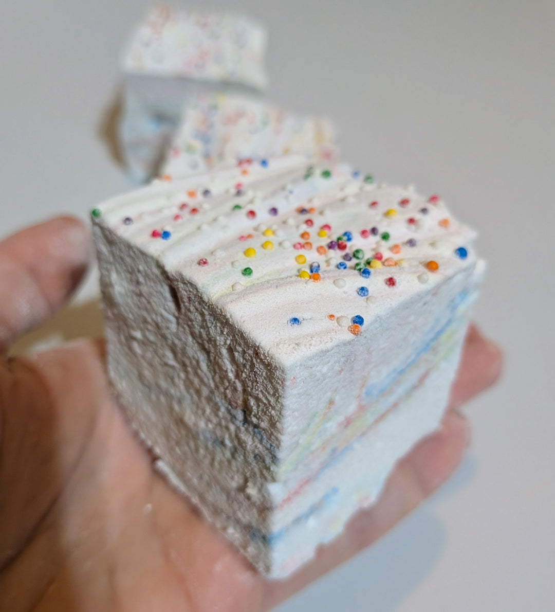 Close-up of a Tutti Frutti gourmet marshmallow held in hand, showcasing rainbow sprinkles and soft, pillowy texture. Handcrafted by The Toasty S’more with organic marshmallow root, beef gelatin, and no corn syrup, this jumbo 2-inch cube is a colorful, gluten-free treat made in USA.