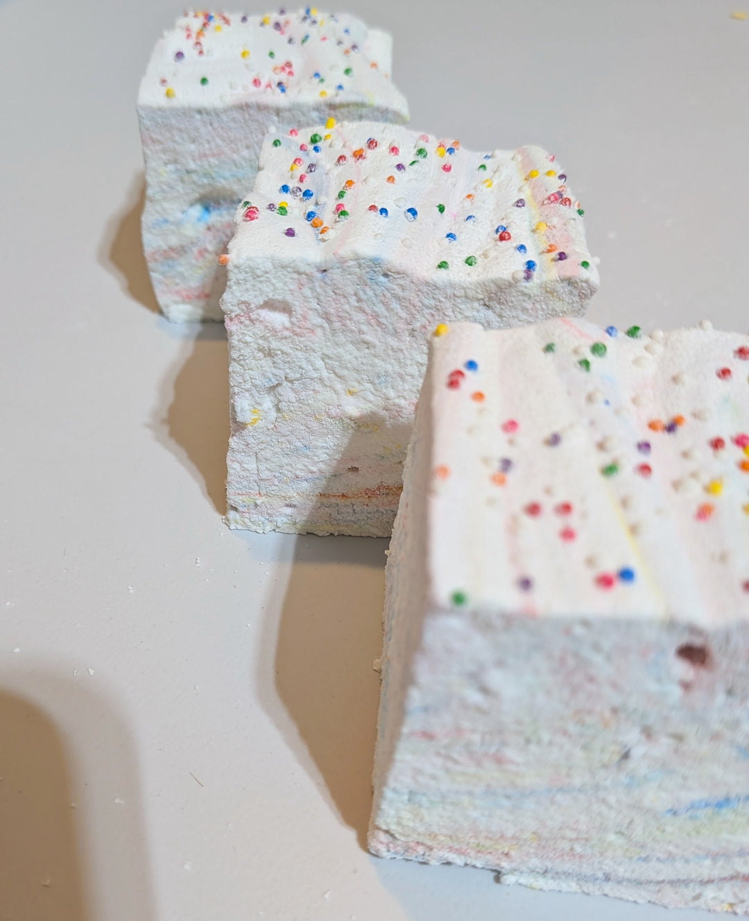 Close-up of a jumbo Tutti Frutti marshmallow topped with rainbow sprinkles, highlighting its soft texture and vibrant fruity layers. Handcrafted by The Toasty S’more with organic marshmallow root, Halal beef gelatin, and no corn syrup, natural colors, this colorful 2-inch cube is a clean-label treat made in Texas.