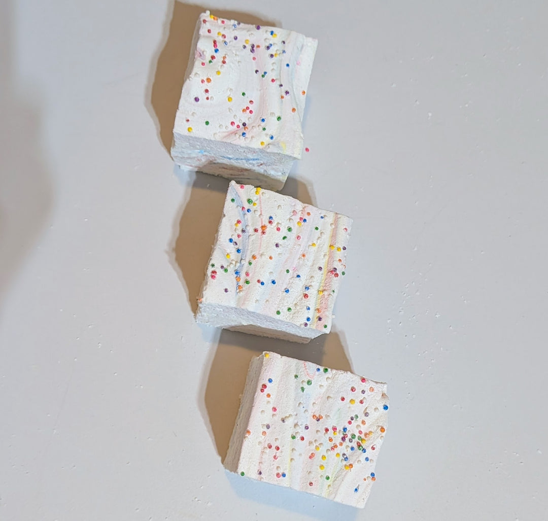Top-down view of three jumbo Tutti Frutti marshmallows with rainbow sprinkles, arranged on a clean white background. Handcrafted by The Toasty S’more with organic marshmallow root, beef gelatin, and no corn syrup, natural colors, these colorful 2-inch cubes offer a fruity, gluten-free treat perfect for gifting or snacking.

