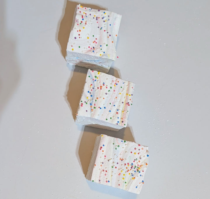 Top-down view of three jumbo Tutti Frutti marshmallows with rainbow sprinkles, arranged on a clean white background. Handcrafted by The Toasty S’more with organic marshmallow root, beef gelatin, and no corn syrup, natural colors, these colorful 2-inch cubes offer a fruity, gluten-free treat perfect for gifting or snacking.

